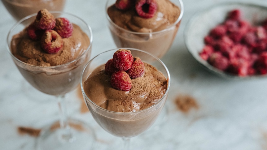 Three stemmed glasses filled with vegan chocolate mousse, with raspberries and Milo sprinkled on top.