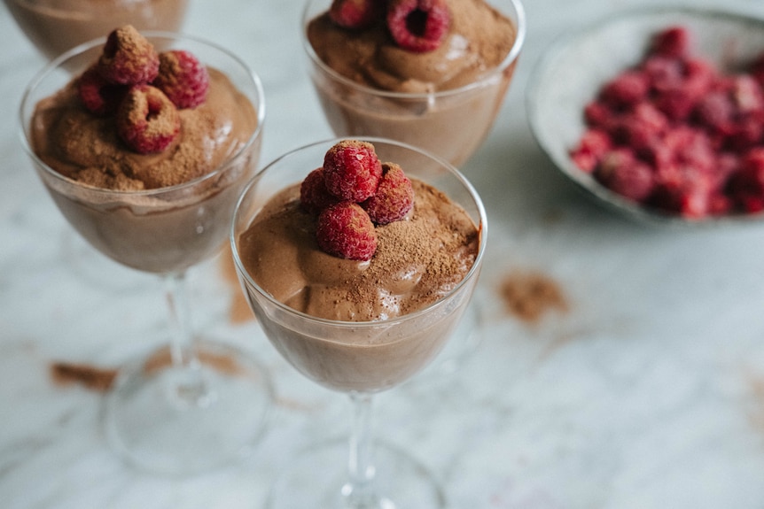 Three stemmed glasses filled with vegan chocolate mousse, with raspberries and Milo sprinkled on top.