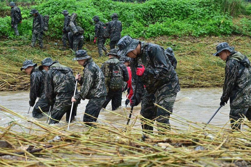 South Korean marines use thin poles to search knee high brown floodwaters for missing people.