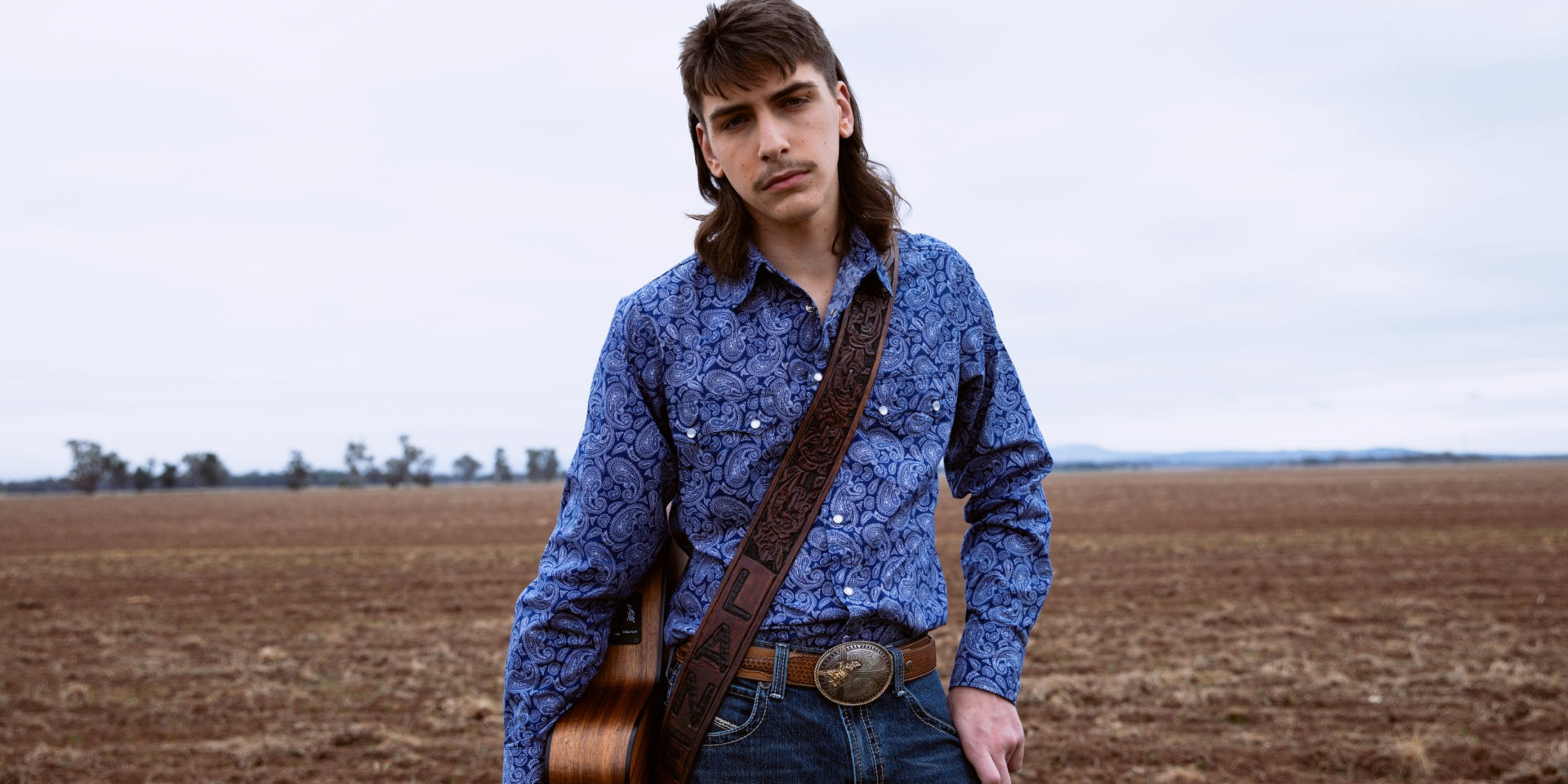 Um homem em um campo com um violão pendurado sobre o corpo.