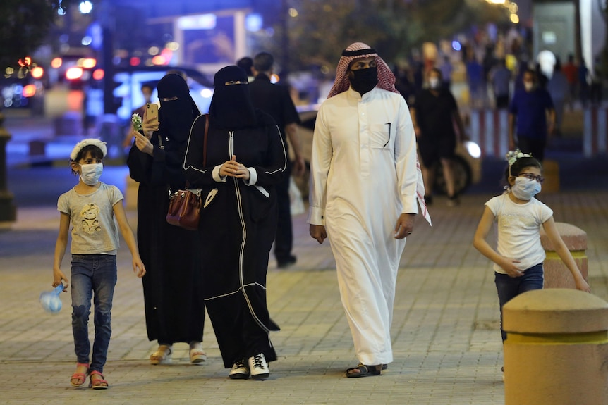 一个戴着防护口罩和传统服装的沙特家庭走在街上。
