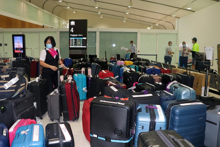 A woman stands next to a large number of travel bags