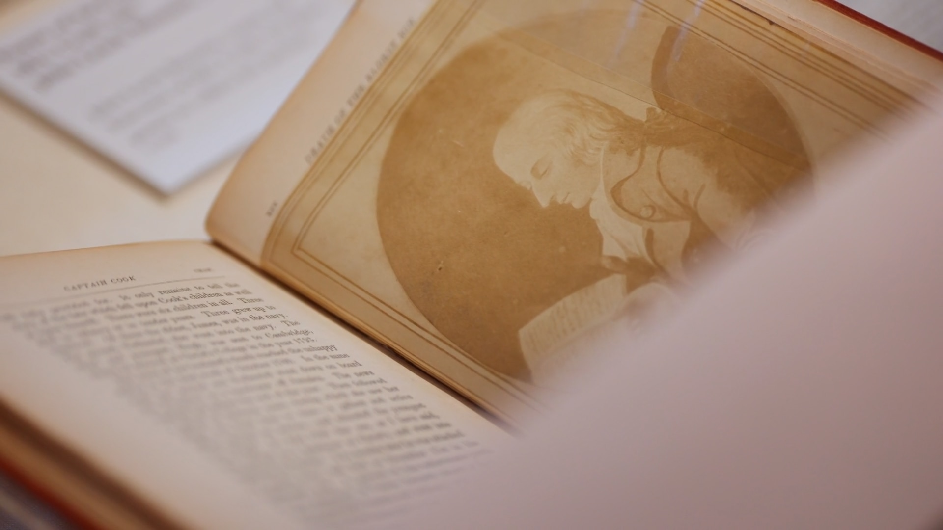 An illustration of Captain Cook in a book on one page, with text on the other.