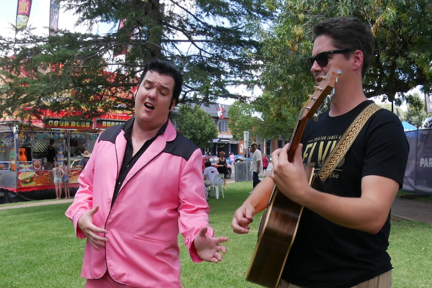 A man in a pink Elvis costume with a man playing a guitar.