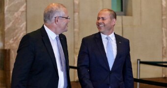 Scott Morrison and Josh Frydenberg smile as they walk in the foyer of Parliament House.