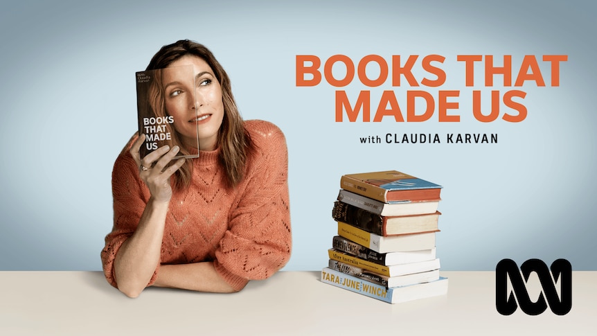 A middle-aged brunette woman holds a book up to her face, the book is a picture of half of her face. She sits beside more books.