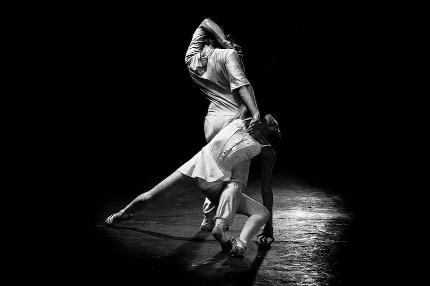 A female dancer is draped over her fellow dancer on stage