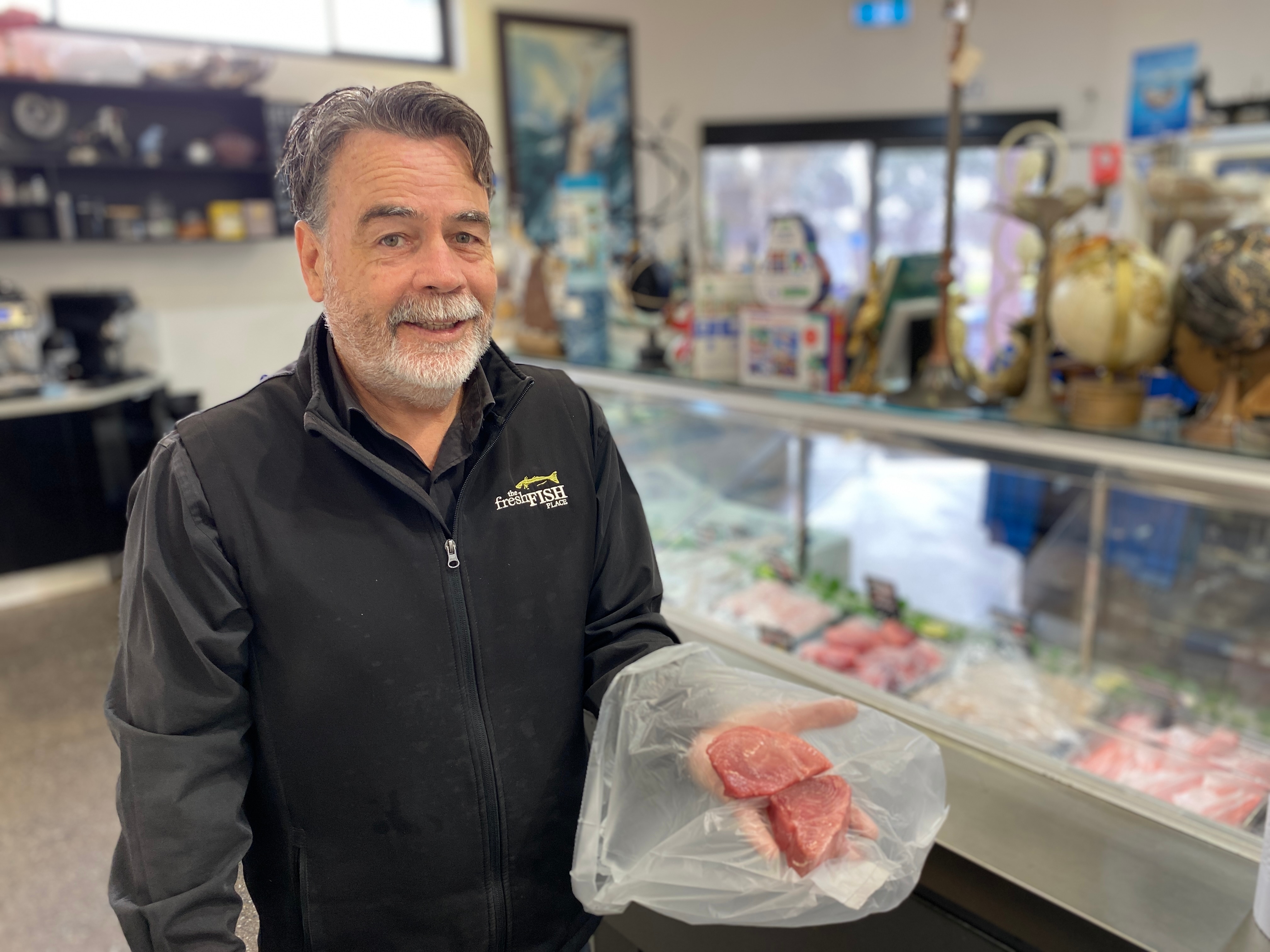 Un hombre con un filete de atún se encuentra en el mostrador de una pescadería y mira a la cámara.