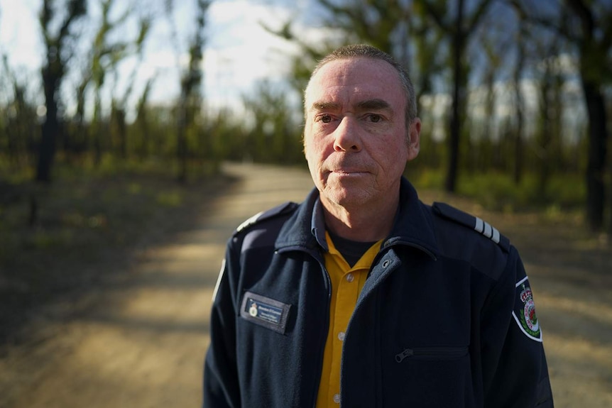 A man in uniform in front of burnt trees.