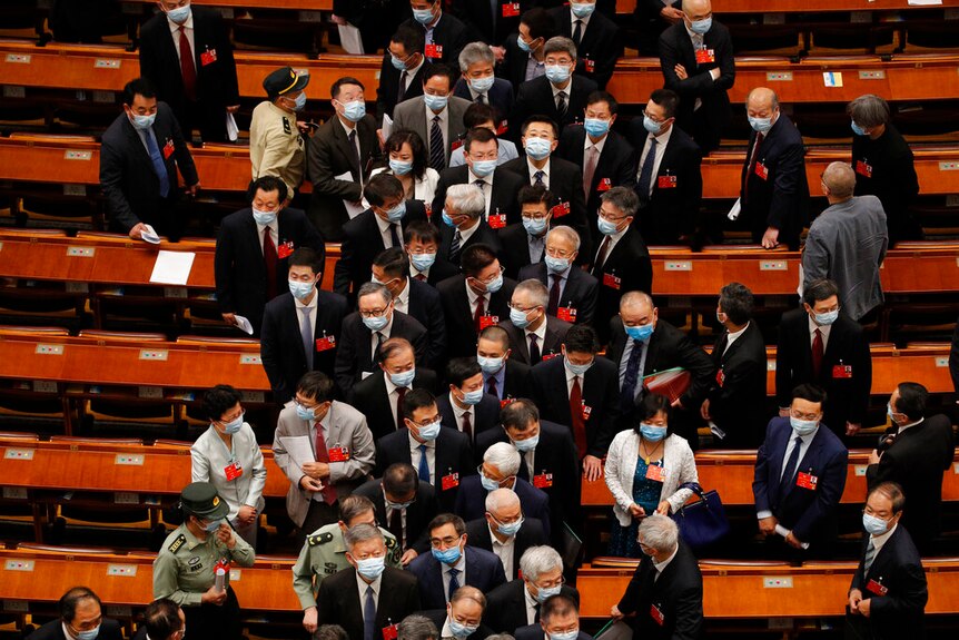 From a high angle, you look down at a crowd of people in suits and face masks trying to exit a narrow conference aisle.