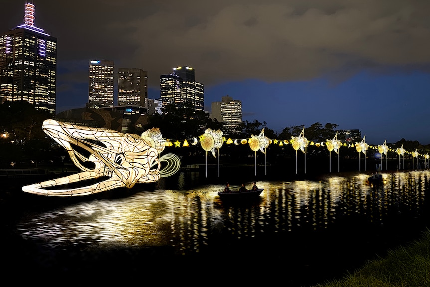 The figure of an eel over a river made of glowing lanterns and lights.