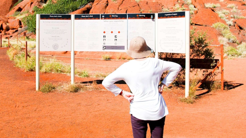 Penny Campbell stands in front of the sign in front of Uluru warning tourists about climbing up