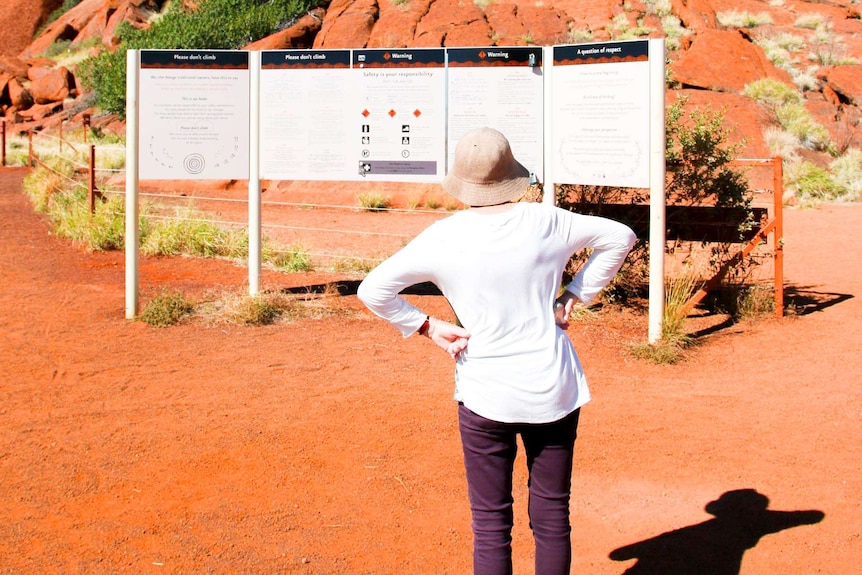 Penny Campbell stands in front of the sign in front of Uluru warning tourists about climbing up