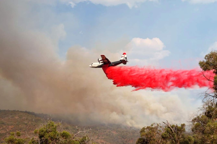 A large aerial tanker drops fire retardant over a bushland area.