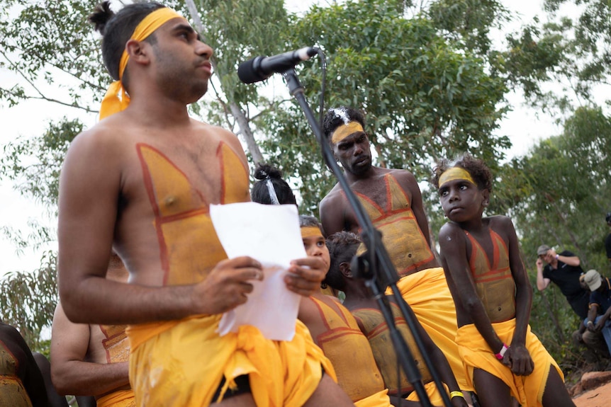 The boy looks up at Michael as he addresses the crowd, both of them in traditional colours of their clan.