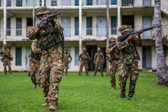 Officers in camouflage pointing guns moving toward camera during a training exercise with a building behind them