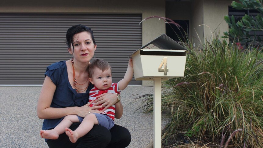 A woman and a baby stands in front of a post box.