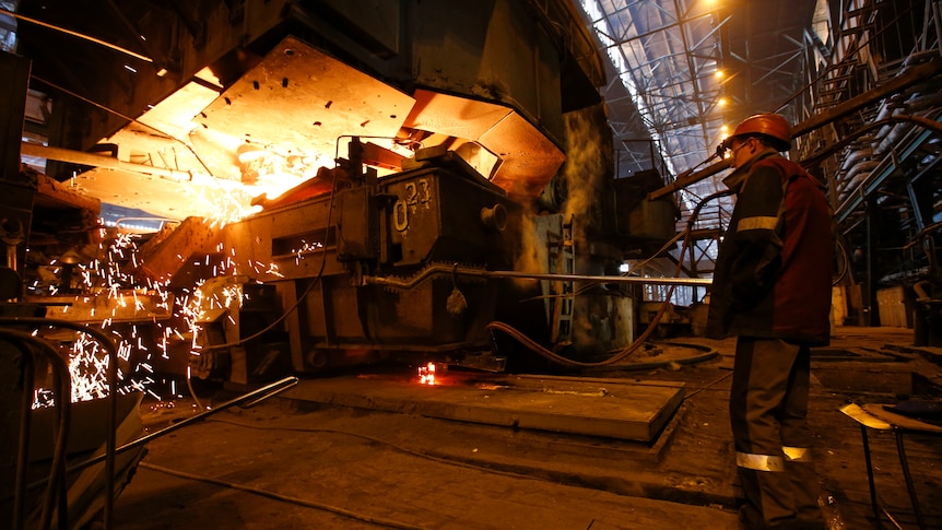 A worker stands next to a metallurgical machine in a factory. 