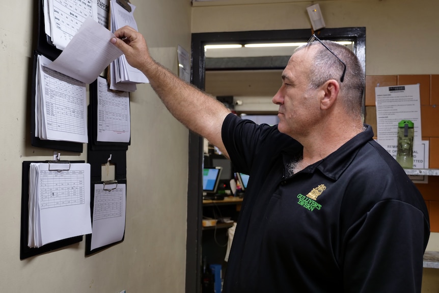 A man checks papers attached to a noticeboard.