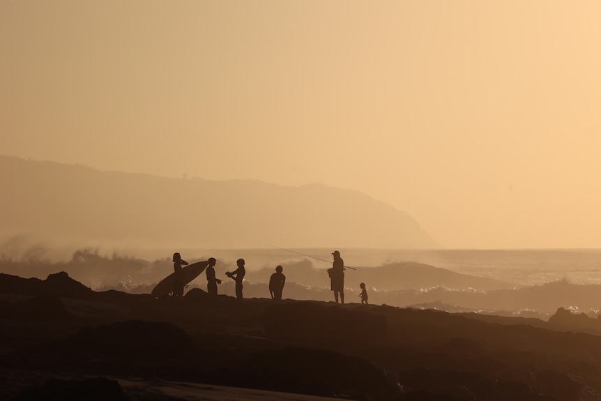 A man and kids silhouetted against the setting sun.
