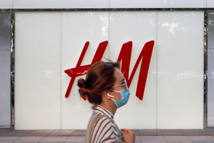 A woman in a face mask walks past the window of an H&M store