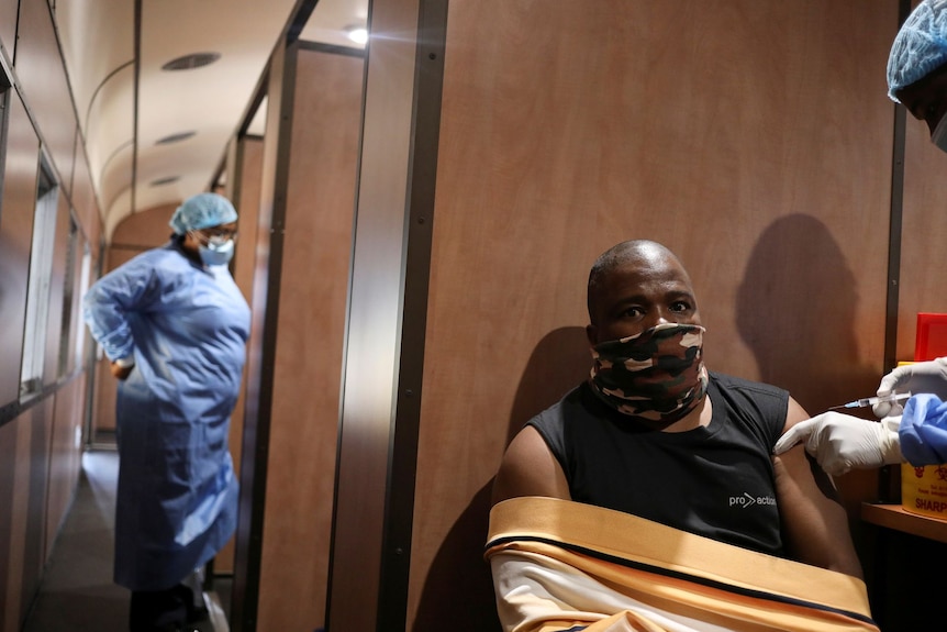 A man receives a vaccine while a health worker behind looks inside a room on a train 