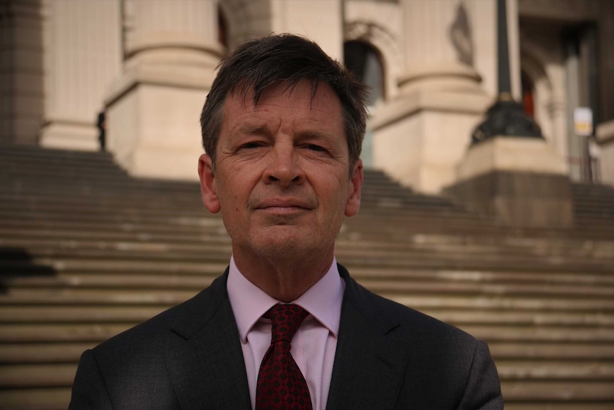 Luke Donnellan stares into the camera while standing on the steps of Victoria's Parliament building