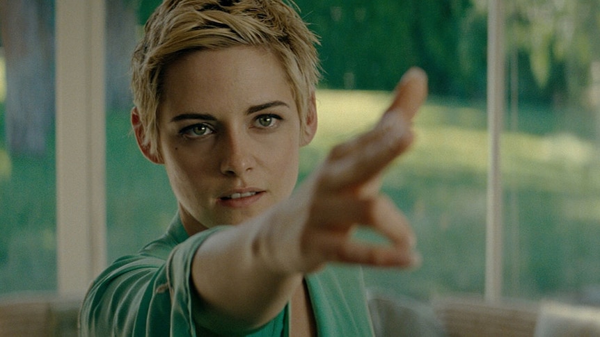 Kristen Stewart with short blonde pixie cut pointing hand towards right of frame with her fingers as gun.