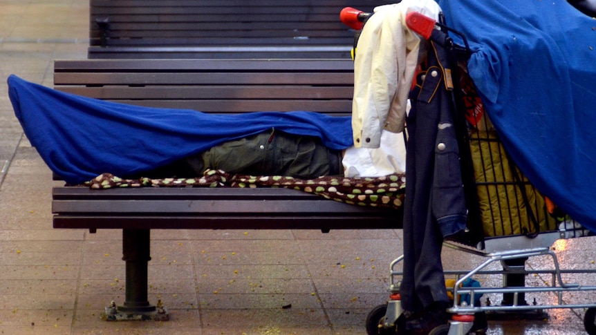 A homeless person lies on a seat.