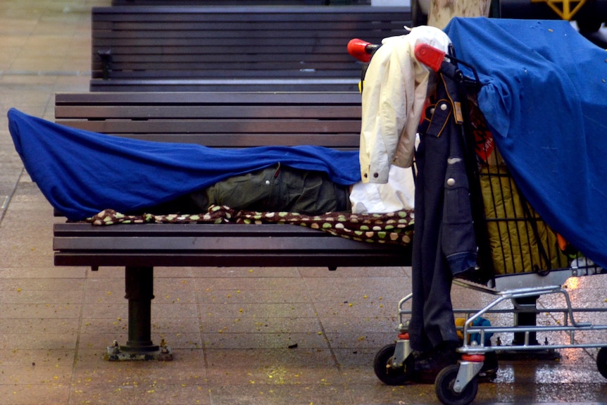 A homeless person lies on a seat.