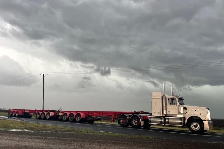 A grey storm cloud sits above a truck parked on the side of a road.