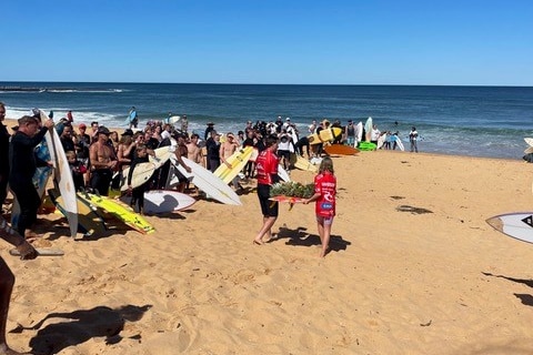 Chris Davidson's children walking a surfboard with a wreath towards the water