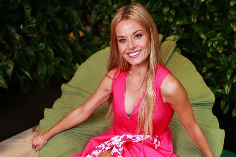 A woman with strawberry blonde hair wearing a pink dress sitting on a chair that looks like a leaf