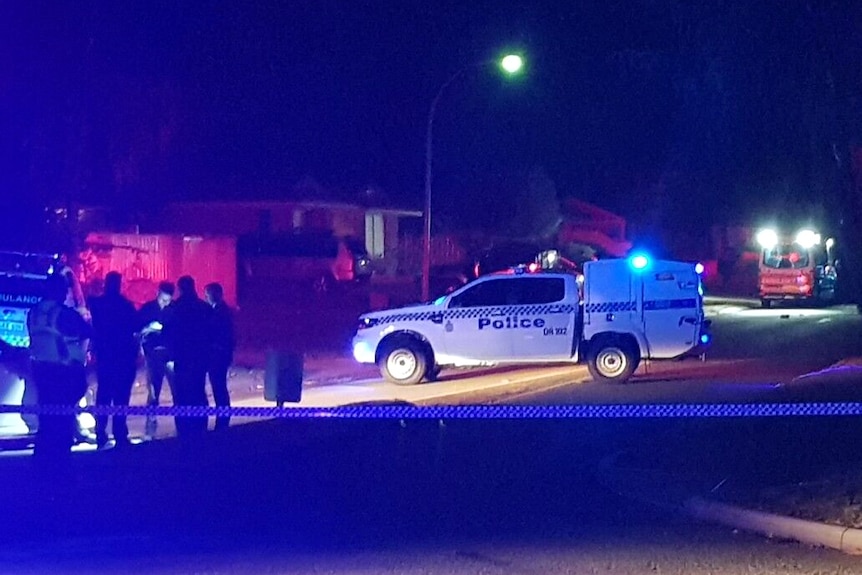 A crime scene on a suburban street in Warnbro at night with a police car and tape blocking the road and officers nearby.