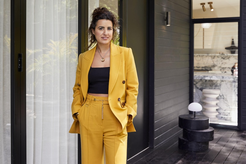 Yasmine Ghoniem wearing a mustard yellow two piece suit with a black top, her hands are in her pockets
