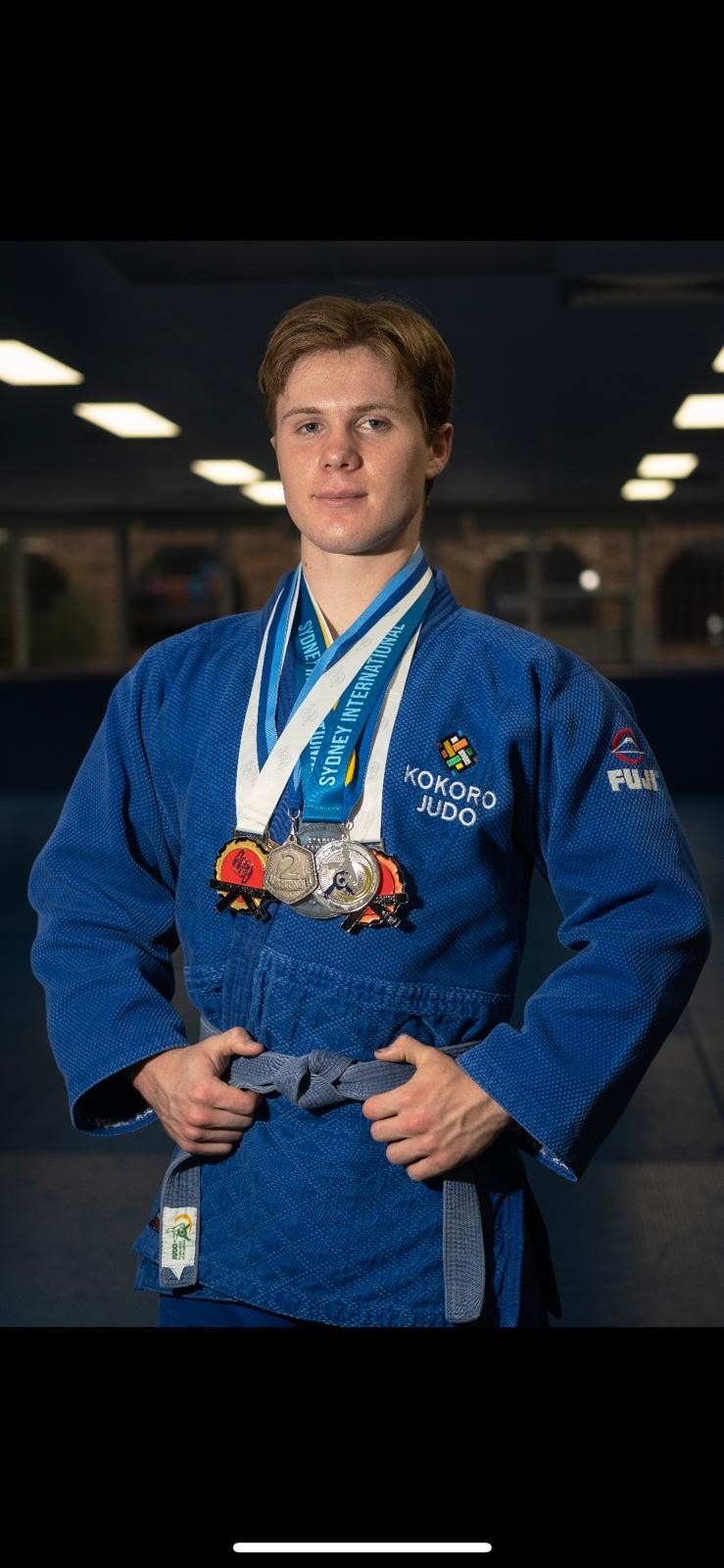 Byron McIntosh is wearing a blue judo outfit. He has multiple medals around his neck.