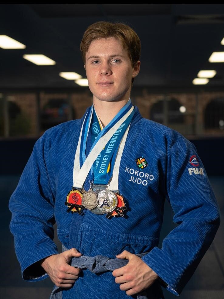 Byron McIntosh is wearing a blue judo outfit. He has multiple medals around his neck.