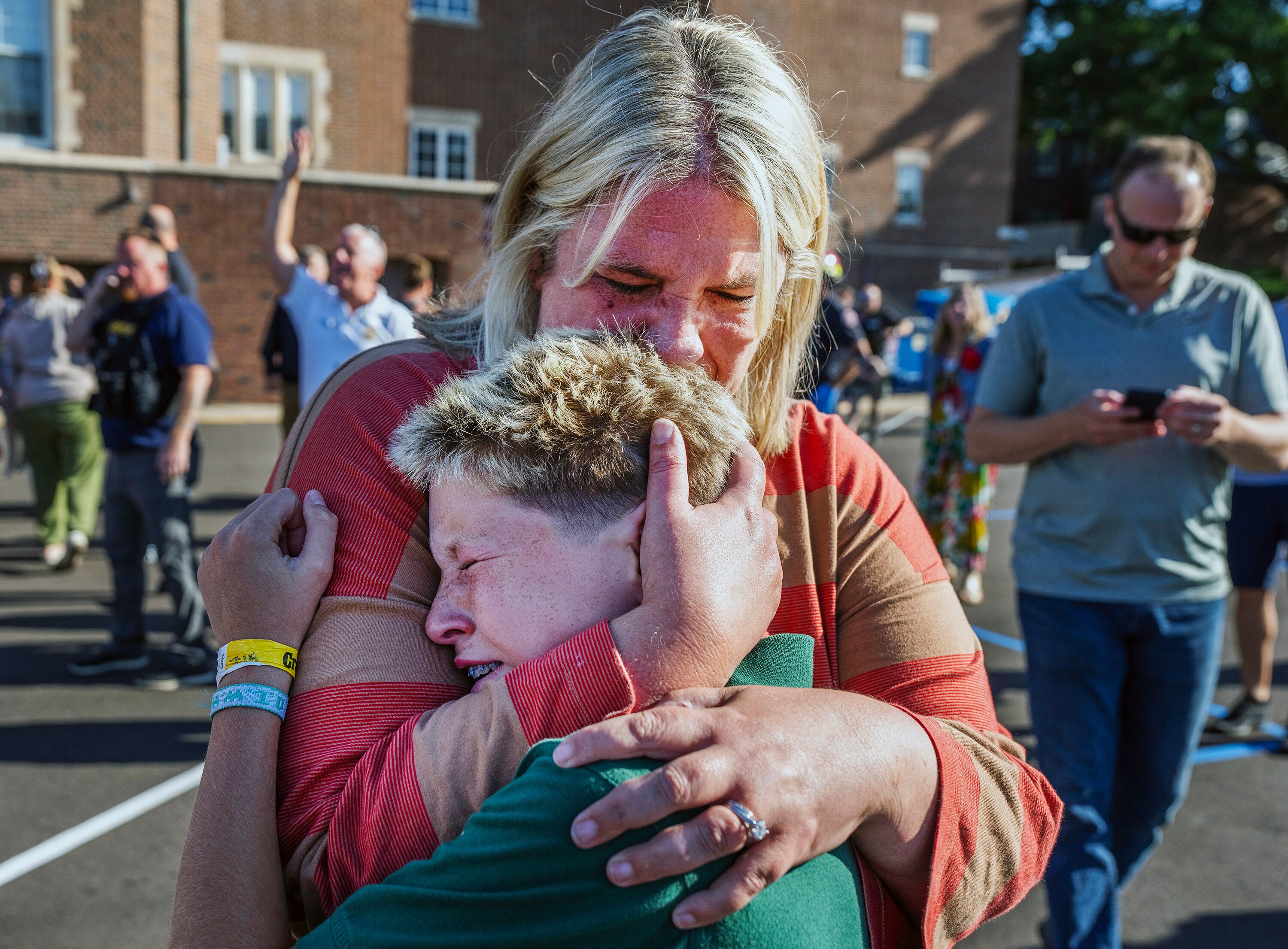 A mother hugging her son out the front of a school building.