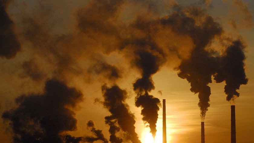 Smoke rises from chimneys of a factory during sunset.