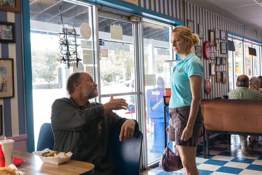 A man holds his hand out to a woman who is standing in a diner