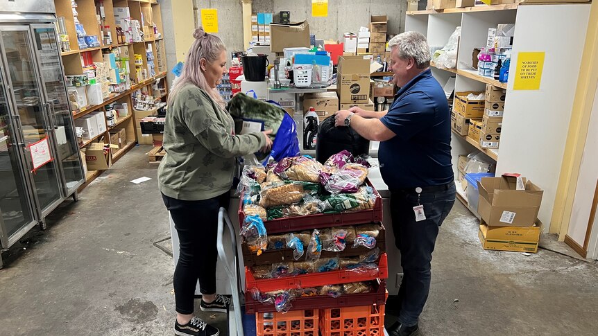 A woman and a man stand in a large storage space, sorting through donated food.