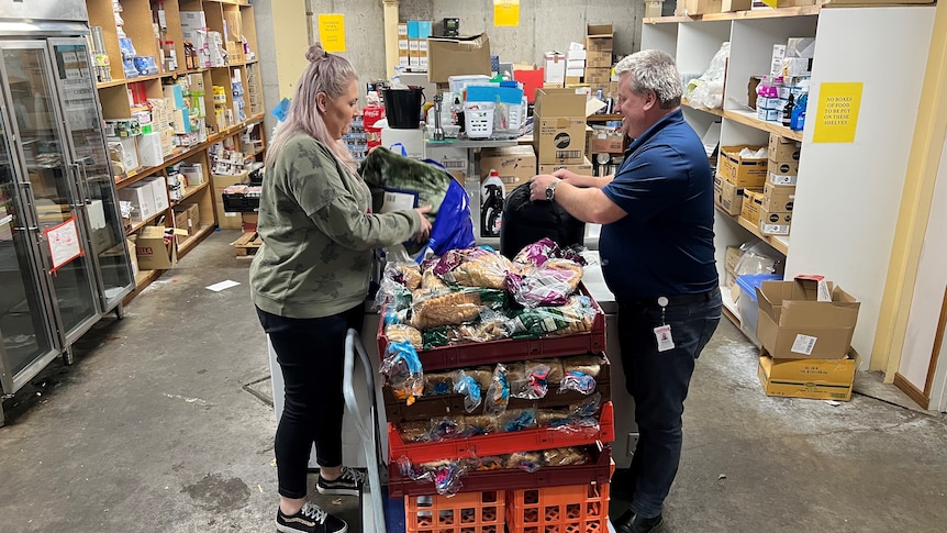 A woman and a man stand in a large storage space, sorting through donated food.