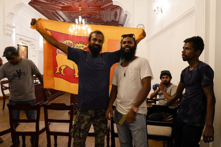 Two men hold up a flag in a room while others watch on.