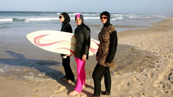 Islamic swimwear worn by three women holding a surfboard