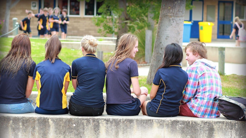 Teenagers sit together with their backs turned