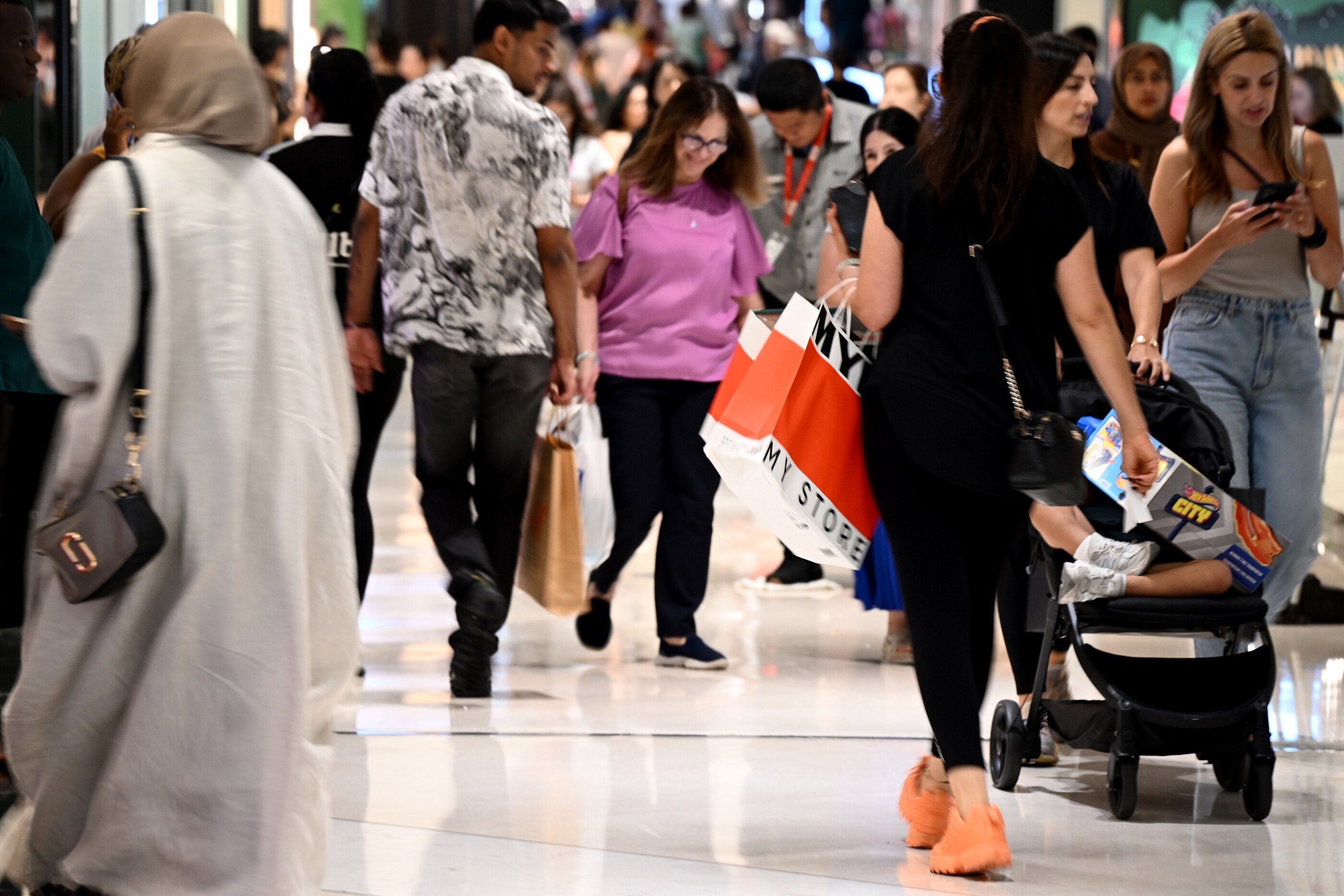 A crowd of people inside a shopping centre carrying shopping bags.