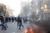 A rubbish bin burns as a protester runs past in Tehran