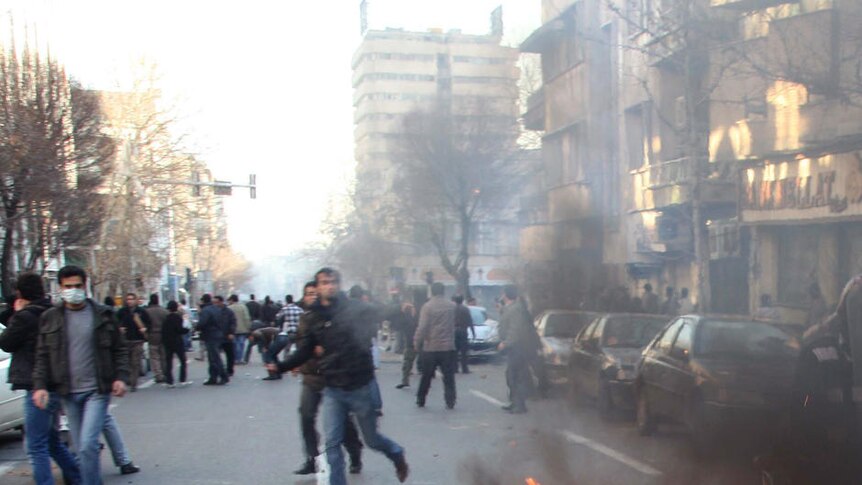A rubbish bin burns as a protester runs past in Tehran