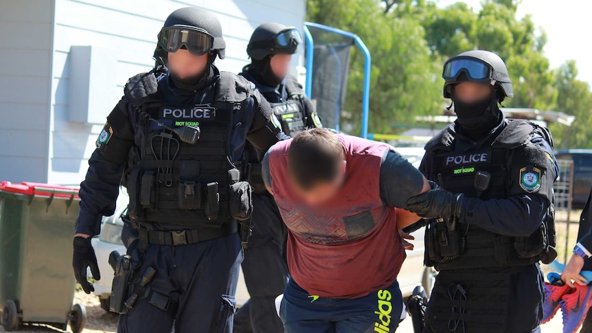 Three NSW Police riot squad members lead away a man under arrest.