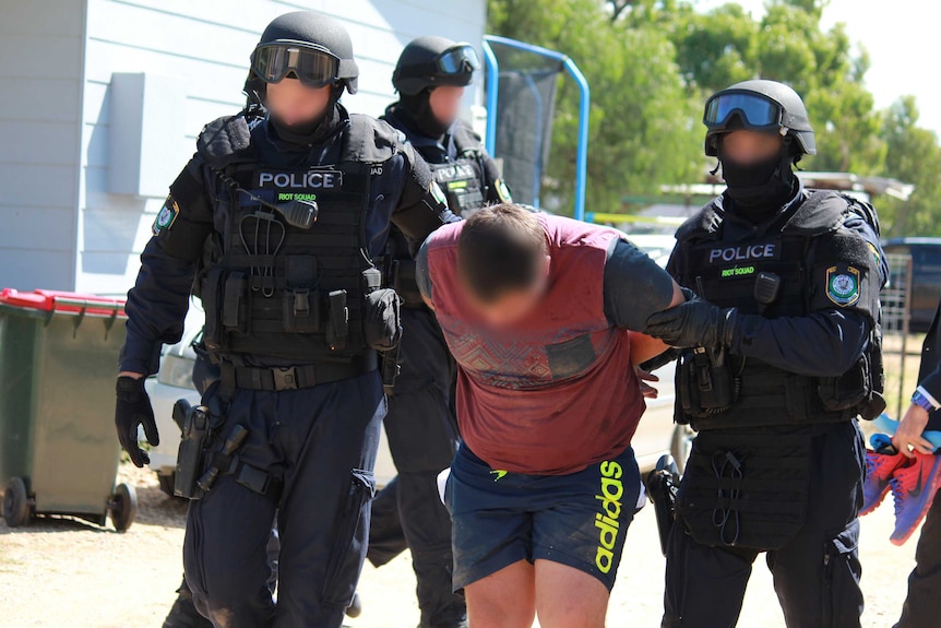 Three NSW Police riot squad members lead away a man under arrest.